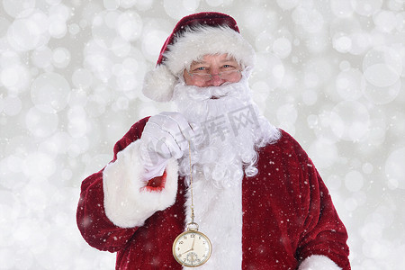 圣诞老人拿着一块大金怀表的特写镜头，带有雪景效果的散景背景。