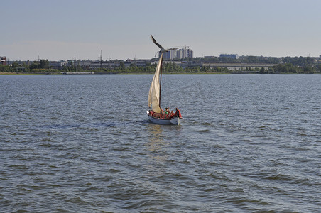 大城市背景下平静湖面上的小帆船。