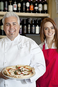 一个快乐的厨师和漂亮的女服务员拿着比萨饼的肖像