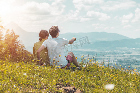 享受田园诗般的山景：情侣坐在田园诗般的草地上，欣赏遥远城市萨尔茨堡的景色