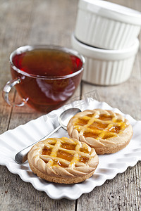 新鲜出炉的馅饼，配上果酱或杏酱，装在白色陶瓷盘上，一杯茶放在质朴的木桌上。