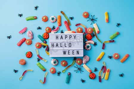 南瓜创意摄影照片_蓝色背景上放着万圣节节日装饰品和糖果，灯箱上写着 Happy Halloween flat