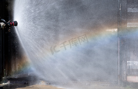 勇敢的消防员摄影照片_关闭消防站洒水器的水幕，在火灾发生区域前反射彩虹。