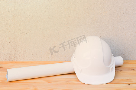带安全头盔摄影照片_白色安全头盔塑料和纸卷计划工程蓝图施工在木地板桌子背景上带复制空间添加文本