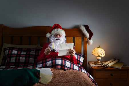 圣诞老人在他位于北极的家中的床上，在烛光下读信。