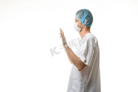 一位男医生举起双手站立，戴着手套，头戴面具和帽子，侧视