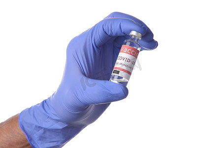 一只手的特写，戴着蓝色乳胶手术手套，手里拿着一瓶 Covid-19 疫苗。