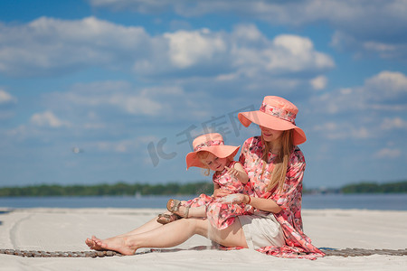 一个小女孩和她妈妈穿着相配的漂亮背心裙在沙滩上玩耍。