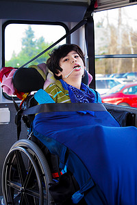 固定不动摄影照片_坐在轮椅上的残疾八岁男孩在校车上扣了