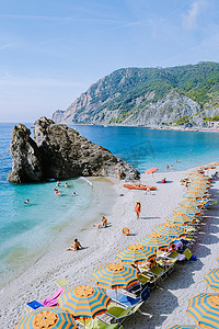 欧洲遮阳伞摄影照片_椅子和遮阳伞填满了 spiaggia di fegina 海滩，这是意大利 Monterosso 宽阔的沙滩村，是意大利五渔村的一部分