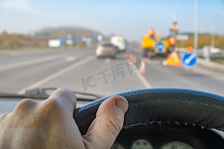 方向盘背景摄影照片_道路工程背景下司机手握汽车方向盘