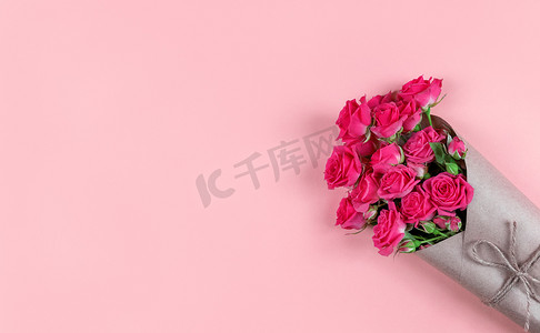 喜庆海报背景摄影照片_一束小花玫瑰，包裹在粉红色背景的牛皮纸中，带有复制空间。