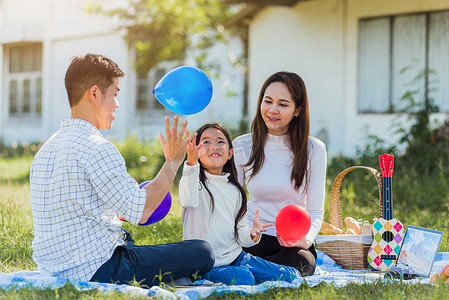 野餐毯摄影照片_坐在野餐毯上玩气球的快乐家庭在户外玩得开心