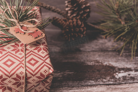 圣诞礼物的特写，包括用红色复古包装纸包裹的创意手工装饰质朴 diy 礼物，用天然复古麻线作为装饰，在旧木地板上装饰，背景是云杉树枝和松果，有复制空间