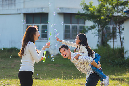 家庭玩乐摄影照片_亚洲家庭母亲、父亲和小女孩一起玩乐，在公园里吹肥皂泡