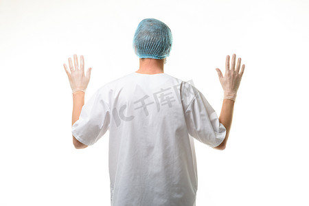 一位男医生举起双手站立，戴着手套，头戴面具和帽子，后视