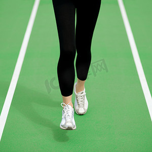 在公路上奔跑摄影照片_女运动员赛跑者脚在绿色跑道上奔跑。