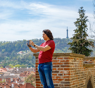 一个男人站在砖墙上拍摄布拉格的全景。