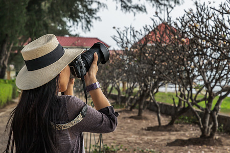 年轻女子戴着白色帽子，拿着相机拍摄海边的风景。