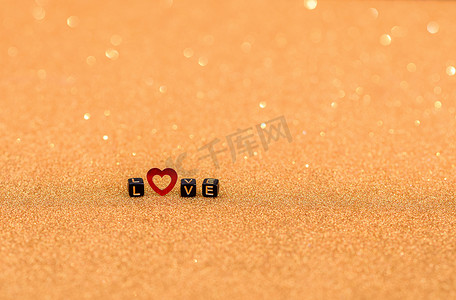 爱这个词是用木制字母和一颗红色的心放在带有亮片的金色背景上的。