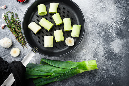烤盘上的生炖韭菜未煮熟，带有香草成分，在带纹理的灰色背景顶视图上，带有文本空间。