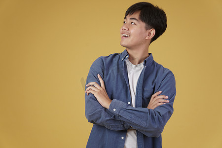 黄色背景中突显的快乐亚洲年轻男子的肖像，穿着随意，双臂交叉