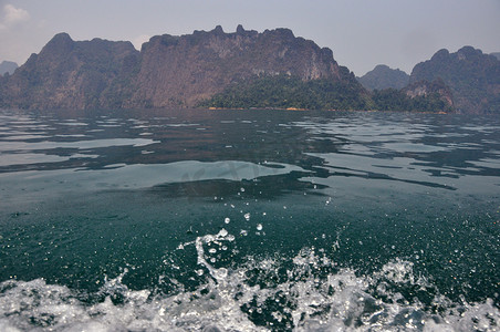 透明清新摄影照片_热带海湾的浪花与悬崖，清澈清新的蓝色清澈的水浪与背景的岩石悬崖，泰国，Khao Sok 国家公园。