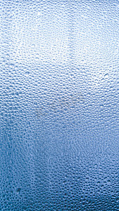 雨天玻璃上的雨滴。玻璃上闪闪发光的水面。水滴呈球状或球状。蓝色雨滴背景。