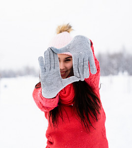 雪天，身穿红色毛衣的漂亮年轻女子在户外用手做框标