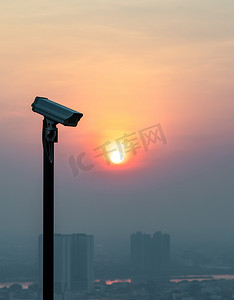 在都市风景和摩天大楼背景的现代监控照相机与太阳在太阳落山前闪耀。