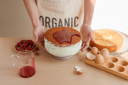 糖浆摄影照片_拿着海绵蛋糕或红色天鹅绒蛋糕的男性糕点师用糖浆或果酱