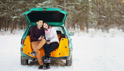 冬天，一对幸福的夫妇坐在汽车敞开的后备箱里，在大自然中