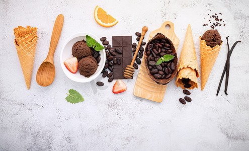 巧克力粒摄影照片_在白色石头背景上设置黑巧克力和可可粒的碗中的巧克力冰淇淋口味。
