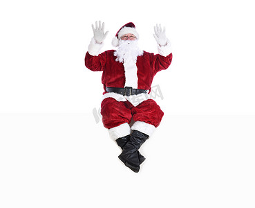 身着传统圣诞老人套装的老人坐在白墙上，双手举在空中。