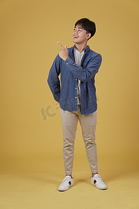 快乐英俊的亚洲年轻男子的肖像，穿着随意，手指指向黄色背景中孤立的复制空间