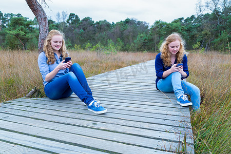 手机操作摄影照片_两个女孩在大自然中操作手机