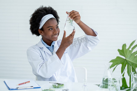 在实验室或教室完成实验后，非洲裔美国年轻女孩拿着并看着里面装有植物的玻璃瓶，并开心地微笑。