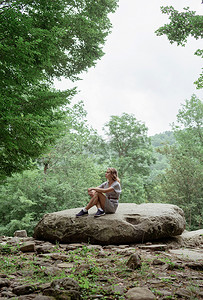 大石摄影照片_穿着夏装的年轻女人坐在森林里的一块大石头上休息或冥想