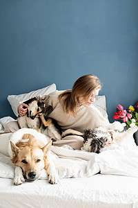 宠物狗玩耍摄影照片_快乐的年轻女人坐在床上和她的狗玩耍