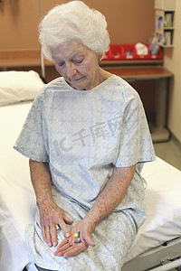 一位穿着病号服的老太太坐在床上，低头看着手里的几颗药丸