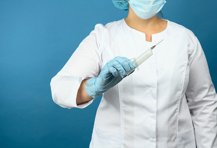 身着白色医用大衣和面具的医生站在蓝色背景上，拿着塑料注射器，接种疫苗