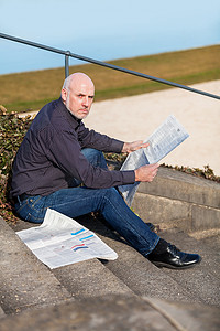 男人坐在台阶上看报纸