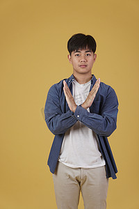 盖中盖表情摄影照片_英俊的亚洲年轻男子的肖像穿着随意地交叉双臂以消极拒绝或在黄色背景中没有表情孤立