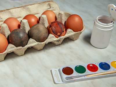 桌子上的罐子摄影照片_在灰色桌子上的刷子、油漆和罐子旁边的盒子里画鸡蛋