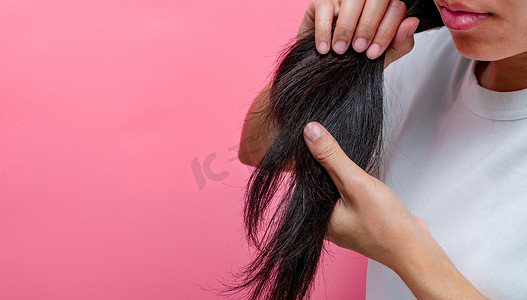 亚洲女人嘴唇干燥，在粉红色的背景下拿着受损的头发。