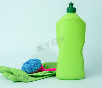 蓝色背景塑料瓶中用于清洁和清洁液的绿色橡胶手套