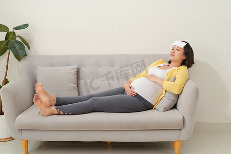 腹疼摄影照片_孕妇肚子疼躺在家里的沙发上