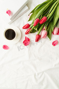 白色床上的粉色郁金香、咖啡杯和书籍