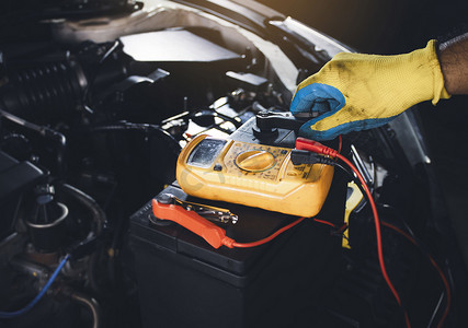 用数字万用表检查汽车电池电压的技术人员夹紧跨接电缆