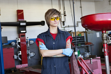 车间一名身穿防护服、双臂交叉的年轻女机械师画像